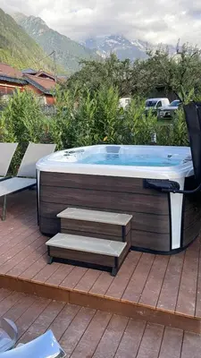 a hot tub on a deck with a chair and stairs at Chalet avec Jacuzzi vue Dômes de Miage in Bionnay