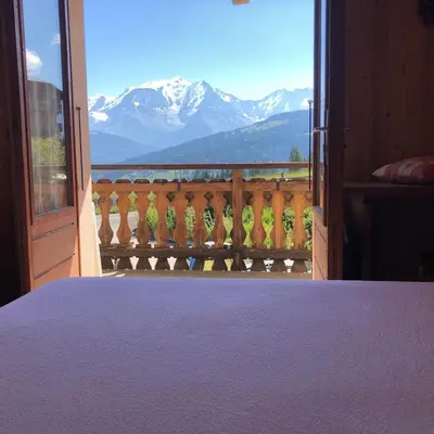 a bedroom with a balcony with a view of mountains at Appartement 10 personnes au pied des pistes vue Mont Blanc in Combloux
