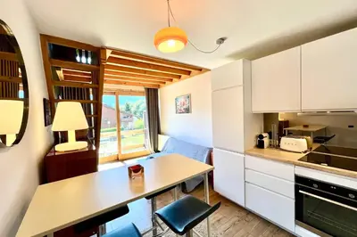 a kitchen with white cabinets and a table with a chair at Le 2ème Ciel in Megève