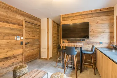 a kitchen with wooden walls and a bar with stools at Studio Berrier - Welkeys in Megève