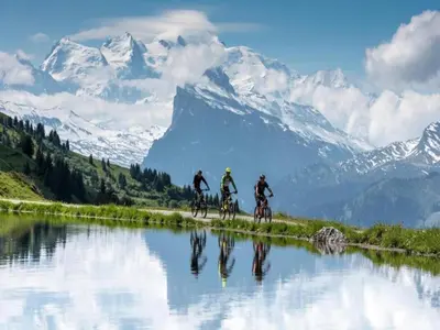 three people riding bikes across a body of water with mountains at Mountain Retreat for Families in Samoëns