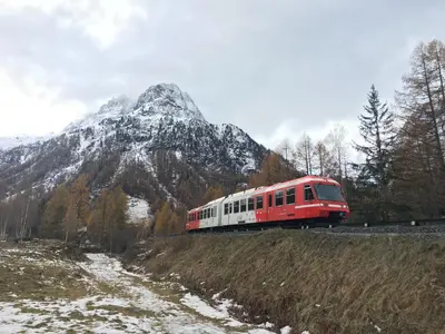 a red and white train traveling past a mountain at Nos Maisons Cosy - Vallorcine in Vallorcine