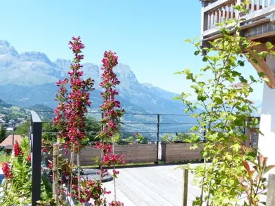 two towers of flowers on a balcony with mountains in the background at Modern Chalet Near Megève With Somptuous Views in Combloux