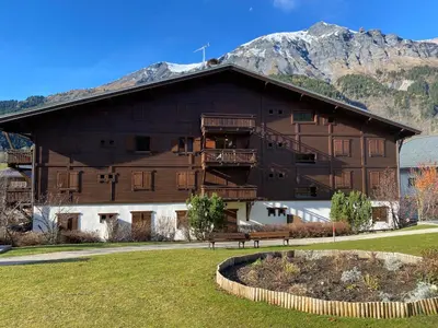 a large wooden building with mountains in the background at Appartement 4-6 personnes centre Les Contamines Montjoie in Les Contamines-Montjoie