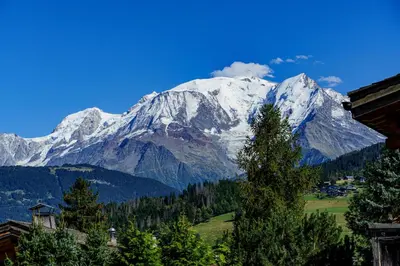 a snow covered mountain range with a house and a lake at Chalet des Sommets in Combloux