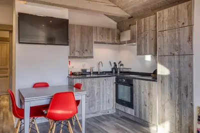 a kitchen with wooden cabinets and a table with red chairs at Séjour lumineux avec vue sur les cimes in Megève