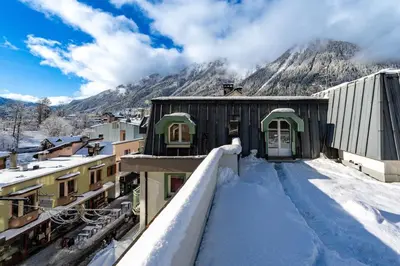 a snow covered balcony with a house and mountains at Hyper central apartment with rooftop in Chamonix-Mont-Blanc