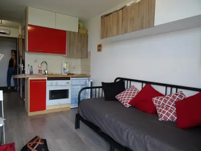 a room with a bed and a kitchen with red cabinets at Studio Samoens 1600 pied des pistes in Samoëns