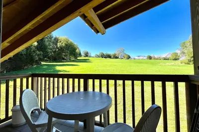 a table and chairs on a porch with a view of a field at Le Grenier du Feug in Combloux