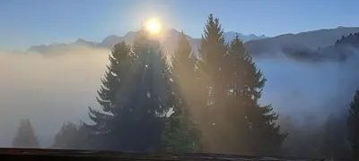 a sun rising on top of a tree covered mountain at AP-37 La Grande Cordée Combloux in Combloux