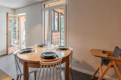 a dining room with a wooden table with chairs and windows at Au coin du feu - Terrasse - Vue Mont Blanc in Saint-Gervais-les-Bains