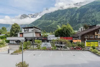 a building in the snow with mountains in the background at Clos Du Savoy - South Facing Balcony - Happy Rentals in Chamonix-Mont-Blanc