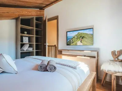 a bedroom with a white bed with a television on the wall at Chalet Zazen I Le Chalet Club in Combloux