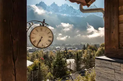 a clock hanging from a building with a view of a mountain at Chalet La Source - Ideal familles ski et rando in Chamonix-Mont-Blanc