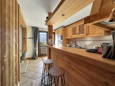 a kitchen with wooden cabinets and a counter with stools at PE317 - 4 pieces 6 a 7 pers proximite centre in Les Carroz d'Araches