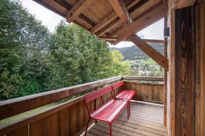 a red bench sitting on a wooden balcony at Luxury Chalet Black Mountain - 4BR, Sleeps 10, Fireplace, Mountain Views & Garden - Megève in Megève