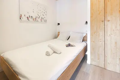 a bedroom with a bed with white sheets and wooden floors at Résidence Les Periades - Chamonix in Chamonix-Mont-Blanc