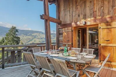 a wooden deck with a table and chairs at Chalet Ysalpe - Vue montagne hammam sauna jacuzzi et salle cinéma in Megève
