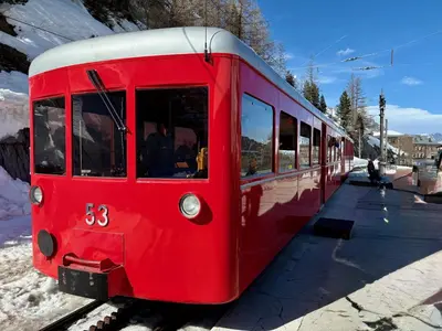 a red train is parked on the tracks at Alpen Lounge in Servoz