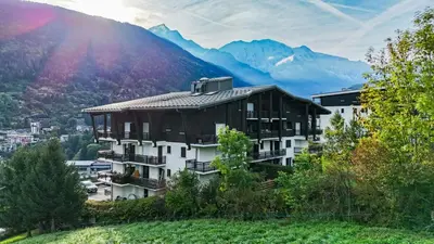 a building on a hill with mountains in the background at Les Cimes de Saint-Gervais apartment in Saint-Gervais-les-Bains