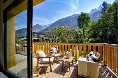 a deck with chairs and a table with mountains in the background at Chalet du Cristal Blanc in Chamonix-Mont-Blanc