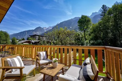 a deck with chairs and a table with mountains in the background at Chalet du Cristal Blanc in Chamonix-Mont-Blanc