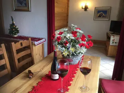 a table with two glasses of wine and a vase of flowers at Chamonix Central Panoramic Apartment & Private Sauna in Chamonix-Mont-Blanc