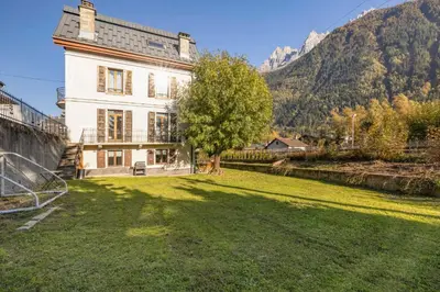 a house with a large yard with a tree and mountains at Nid du Pic - Cozy alpine retreat with private garden in Chamonix in Chamonix-Mont-Blanc