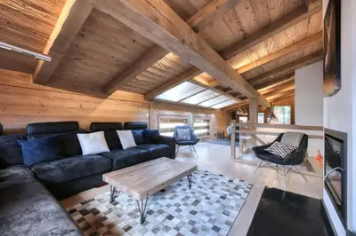 a living room with a black couch and a wooden ceiling at Le Cédron, demi-chalet centre pièton Megève in Megève