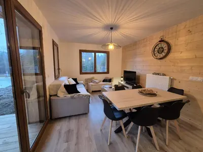 a room with a table and chairs and a living room at Appartement neuf 2 chambres avec parking, rez-de-jardin - FR-1-836-52 in Arâches-la-Frasse