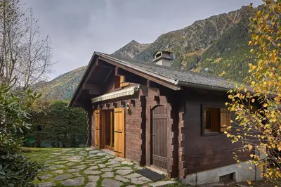 a small wooden house with mountains in the background at Chalet Juno - Chamonix All Year in Chamonix-Mont-Blanc