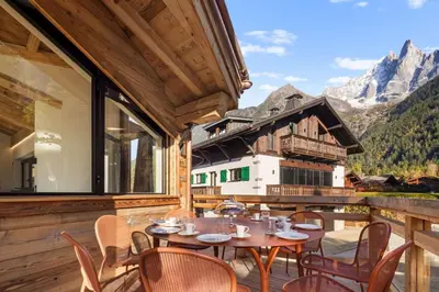 a patio with tables and chairs on a balcony with mountains at Chalet Rémond - Vue Montagnes in Chamonix-Mont-Blanc