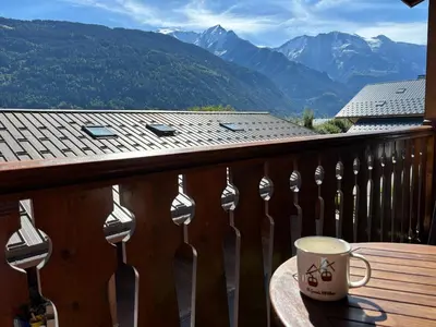 a cup of coffee on a table on a balcony with mountains at La Kabane d'Orsin 3 étoiles in Saint-Gervais-les-Bains