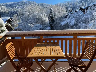 a wooden table and chairs on a balcony with snow covered trees at Duplex neuf 78m², 2 chambres, poêle, WIFI, parking, pour 5 pers. - Arâches-la-Frasse - FR-1-836-57 in Arâches-la-Frasse