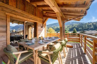 a wooden table and chairs on a deck with mountains at Chalet Les Sapins - Megève in Megève