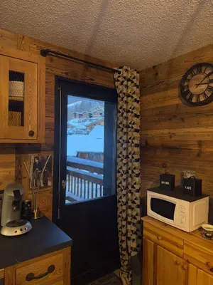 a kitchen with a door to a balcony with a microwave at Studio COCOONING LE CARIBOU in Les Carroz d'Araches
