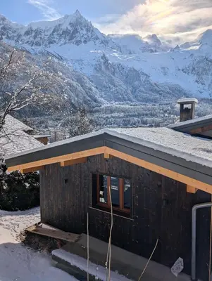 a house with a snowy roof with mountains in the background at Stunning New Apartment in Chamonix with Mont Blanc Views in Chamonix-Mont-Blanc