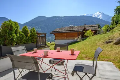 a red table and chairs on a patio with mountains at Le Saint Gervolain in Saint-Gervais-les-Bains