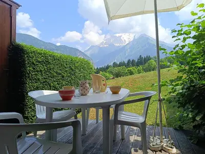 a table with chairs and an umbrella on a patio with mountains at Les hautes Cimes in Saint-Gervais-les-Bains