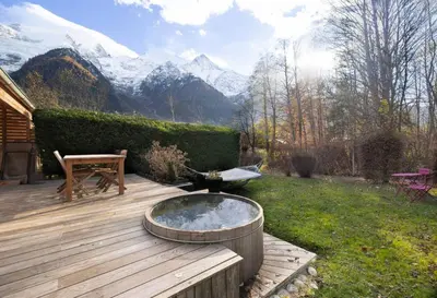 a hot tub on a wooden deck with mountains in the background at Momi Cocon 4pax Jardin Jacuzzi Vue in Chamonix-Mont-Blanc