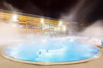 two people swimming in a pool in front of a building at Sapins blancs Megeve in Megève