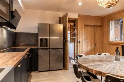 a kitchen with a table and a stainless steel refrigerator at Chalet Paris Mont-Blanc Luxe et authenticite in Saint-Gervais-les-Bains