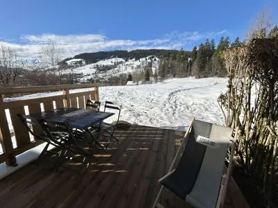 a table and chairs sitting on a deck with snow at Appartement cosy 2 pièces, terrasse, casier à skis, parking commun - FR-1-597-198 in Demi-Quartier