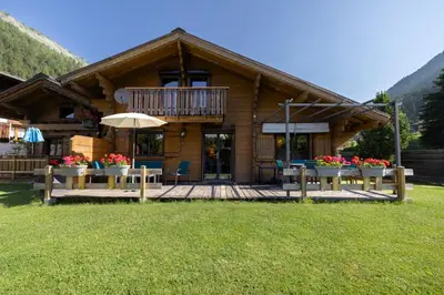 a log cabin with a deck with flowers in front of it at Tete aux Vents - Chalet Familial Centre Vue Randos Parking in Chamonix-Mont-Blanc