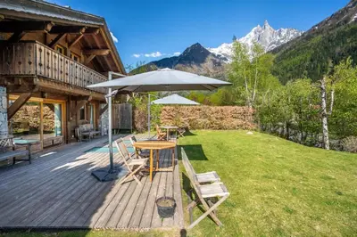 a wooden deck with a table and an umbrella at Michka - Chalet 500m Flegere Cheminee Jardin Vue 180 in Chamonix-Mont-Blanc