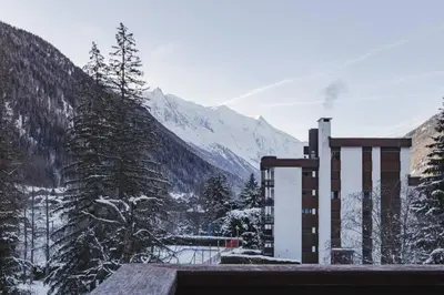 a building with a snow covered mountain in the background at Grand Roc - Cosy Duplex Grands Montets Balcon Vue Parking in Chamonix-Mont-Blanc