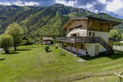 a house in a field with a mountain in the background at Le 111 - Chalet 4CH Calme Vue Pano 5mn Grands Montets in Chamonix-Mont-Blanc