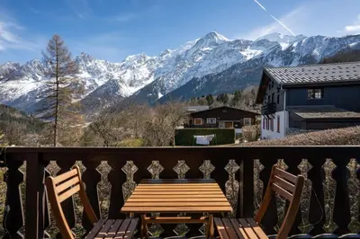 a wooden table and two chairs on a balcony with mountains at Namaste - Cosy 2CH Vue Remontee 500m Parking in Les Houches
