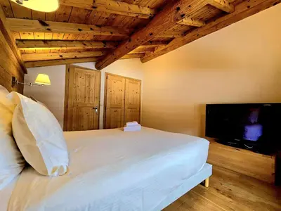 a bedroom with a white bed and a flat screen tv at Charming duplex in Hameau des Pistes ski in ski out in Megève