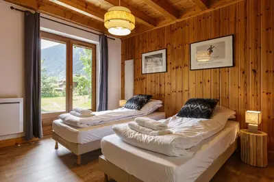 two beds in a room with wooden walls and a window at Arve - Chalet 4CH Jardin Nature Vues BBQ Poele in Chamonix-Mont-Blanc